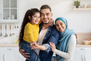 Happy Muslim Parents And Their Little Daughter Posing In Kitchen Interior, Cheerful Islamic Family Of Three Bonding At Home, Middle Eastern Mom, Dad And Child Hugging And Smiling At Camera, Closeup