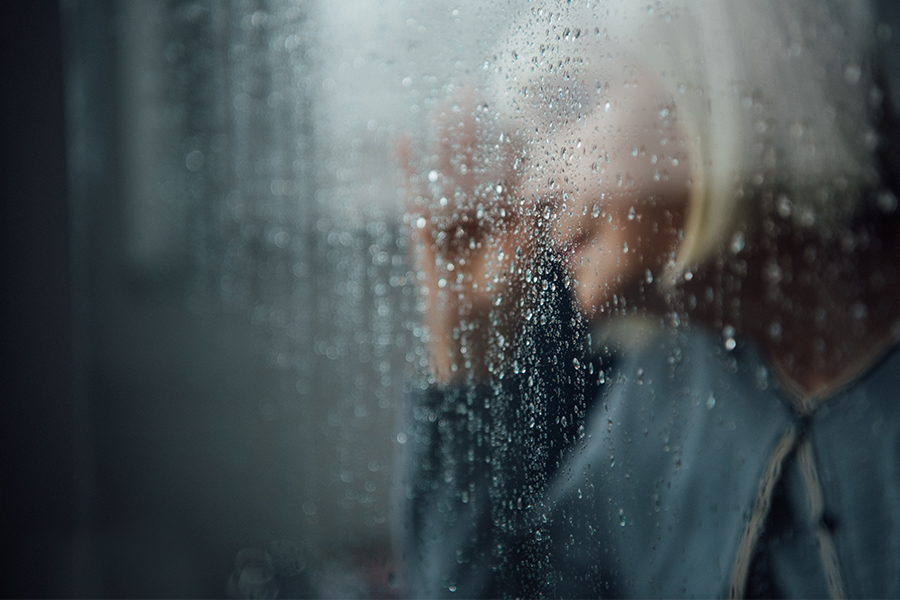 Woman standing at rainy window feeling anxious.